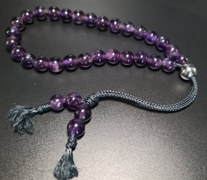 Purple beaded necklace with tassel on a dark surface